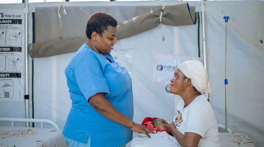 Mwanasaidizi wa uzazi mwanamke mwenye mavazi ya bluu anamtunza mama aliyebeba mtoto wake mchanga ndani ya hema la matibabu huko Burundi.