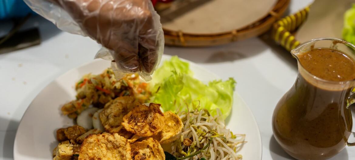 Um close-up de um prato de comida indonésia com satay, tofu, tempeh, brotos de feijão e alface, servido com molho de amendoim.
