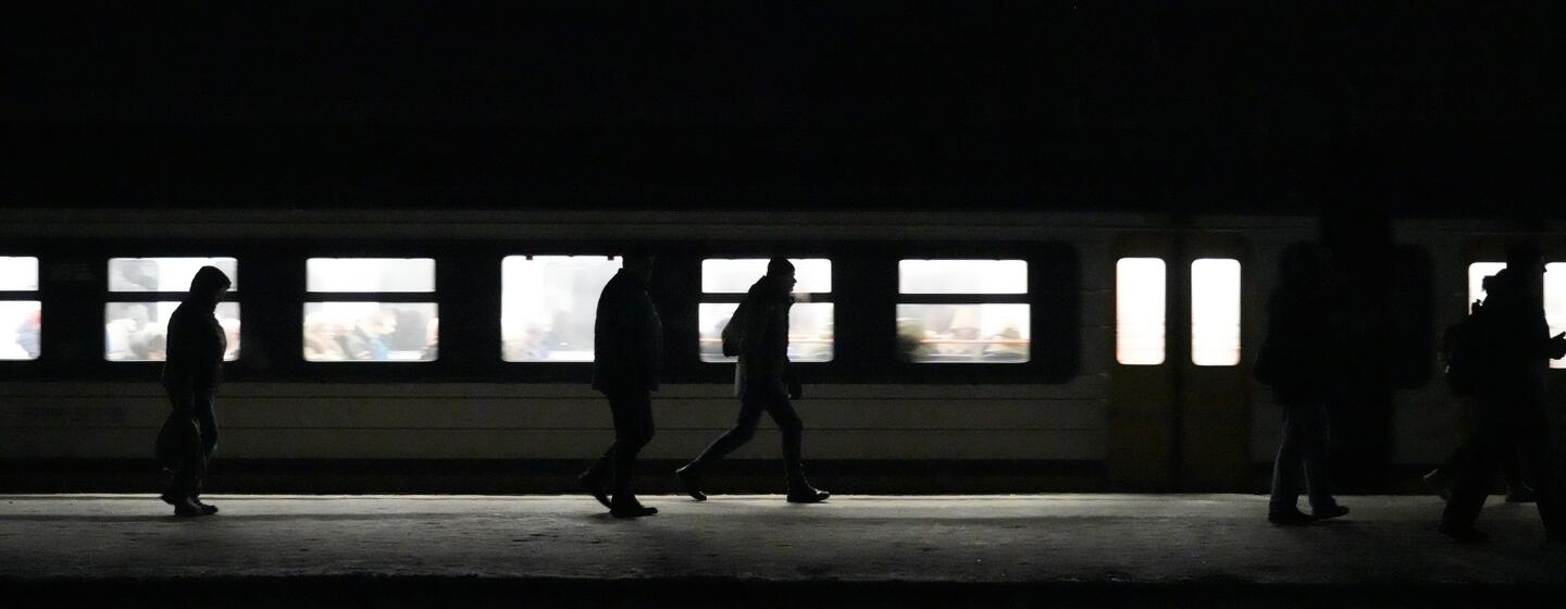 Des silhouettes de voyageurs marchent le long d'un quai de train faiblement éclairé, leurs formes se détachant nettement sur les fenêtres illuminées d'un train.