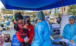 A 5-year-old Venezuelan refugee boy, Deivid, is held by his mother Enyeli during a UNHCR community health event in Lima, Peru. They are receiving vaccinations and medical care alongside other refugee families.