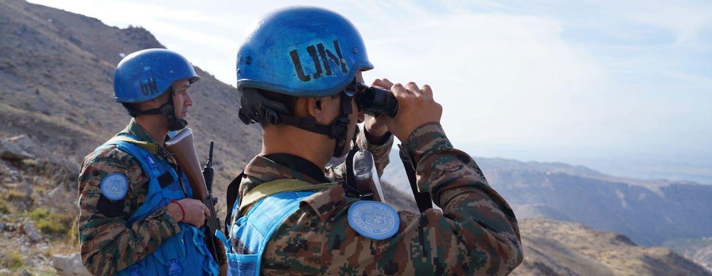 Dois soldados da UNIFIL em capacetes azuis observam a paisagem com binóculos, estacionados ao longo da Linha Azul no Líbano.
