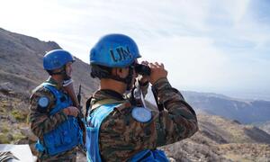 Two UNIFIL peacekeepers in blue helmets observe the landscape with binoculars, stationed along the Blue Line in Lebanon.