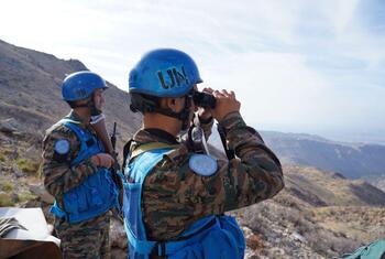 Deux soldats de l'UNIFIL en casque bleu observent le paysage avec des jumelles, stationnés le long de la ligne bleue au Liban.