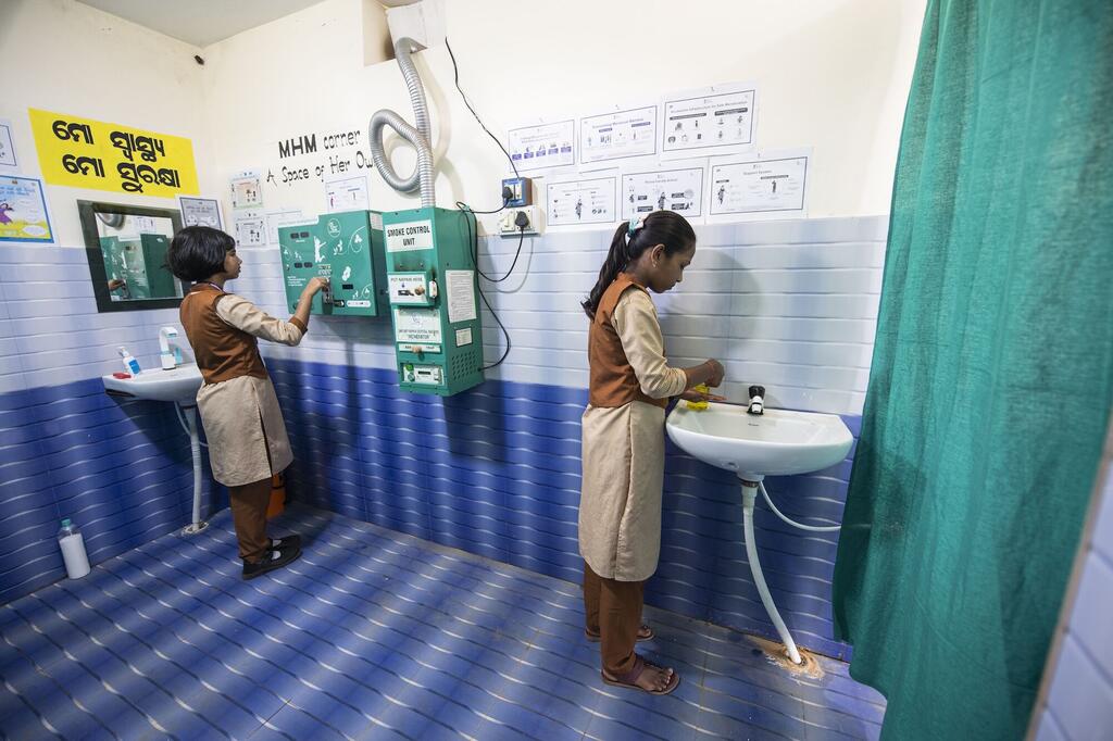 दुतिमेंडी हाई स्कूल की छात्राएँ नए स्थापित माहवारी प्रबंधन (MHM) कोने का उपयोग करती हुईं. इस सुविधा में सिंक, सैनिटरी पैड डिस्पेंसर, ओडिया और आदिवासी बोली में शैक्षिक पोस्टर और नीली टाइल वाली दीवारों वाली एक स्वच्छ, निजी जगह शामिल है.