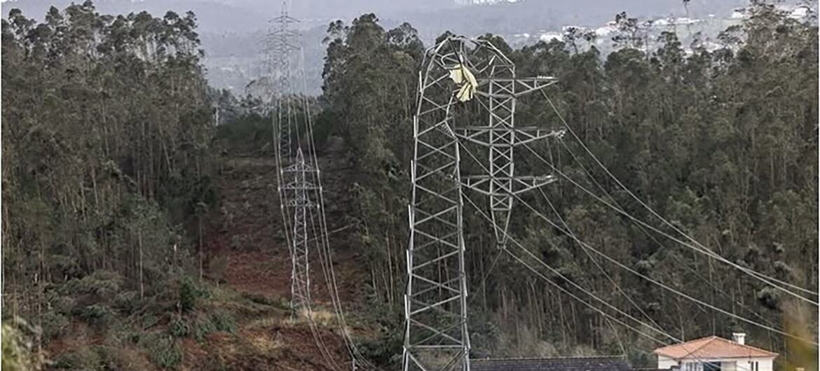 Uma torre danificada de linha elétrica em uma área rural de Portugal após uma tempestade, com casas e floresta no fundo.