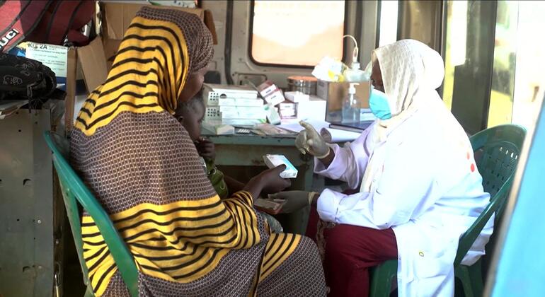 مقدمة رعاية صحية ترتدي معطفا أبيض وكمامة تساعد سيدة سودانية في عيادة متنقلة في أحد مخيمات النازحين في القضارف - السودان