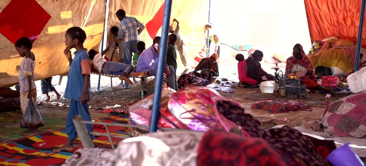 Inside Abu Al Naja camp in Sudan, displaced families, including women and children, rest and move about under large tent structures, highlighting the humanitarian crisis caused by ongoing conflict.