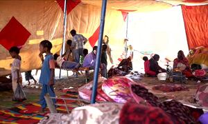 Inside Abu Al Naja camp in Sudan, displaced families, including women and children, rest and move about under large tent structures, highlighting the humanitarian crisis caused by ongoing conflict.