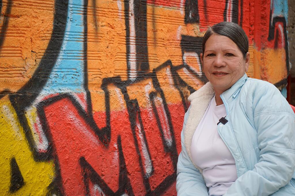 Retrato de Irvin Ibarra, una mujer venezolana que inspira a su comunidad colombiana a través de la danza, de pie frente a un colorido muro de graffiti en Ciudad Bolívar, Bogotá, Colombia.