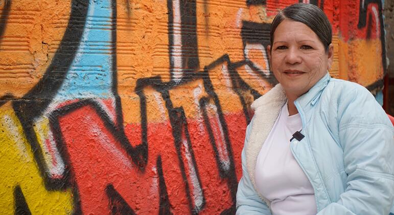 Retrato de Irvin Ibarra, una mujer venezolana que inspira a su comunidad colombiana a través de la danza, de pie frente a un colorido muro de graffiti en Ciudad Bolívar, Bogotá, Colombia.