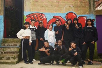 Un grupo de jóvenes colombianos y venezolanos posando juntos frente a un colorido muro de graffiti en el distrito Ciudad Bolívar de Bogotá, Colombia. La imagen captura la integración de la comunidad a través de la danza, destacando la vibrante vida cultural de este barrio urbano.