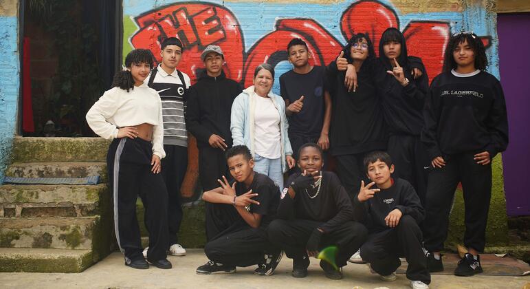 Un grupo de jóvenes colombianos y venezolanos posando juntos frente a un colorido muro de graffiti en el distrito Ciudad Bolívar de Bogotá, Colombia. La imagen captura la integración de la comunidad a través de la danza, destacando la vibrante vida cultural de este barrio urbano.