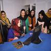 Un grupo de mujeres afganas en un estudio de radio. Una mujer está sentada en un escritorio hablando en un micrófono, mientras otras están alrededor de ella escuchando y sonriendo.