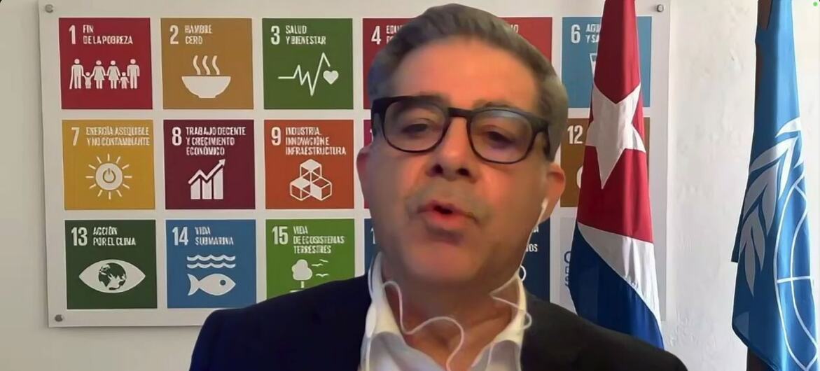 Francisco Pichon, Coordenador Residente em Cuba, fala aos jornalistas sobre a situação no país, diante de um cartaz dos Objetivos de Desenvolvimento Sustentável da ONU e das bandeiras de Cuba e da ONU.