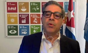Francisco Pichon, Coordinador Residente en Cuba, informa a los periodistas sobre la situación en el país, de pie frente a un cartel de los Objetivos de Desarrollo Sostenible de la ONU y las banderas de Cuba y de la ONU.