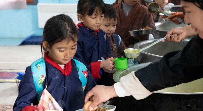 Бутанская школьница в голубой форме получает вареное яйцо из ложки, пока она ждет в очереди за школьным обедом.