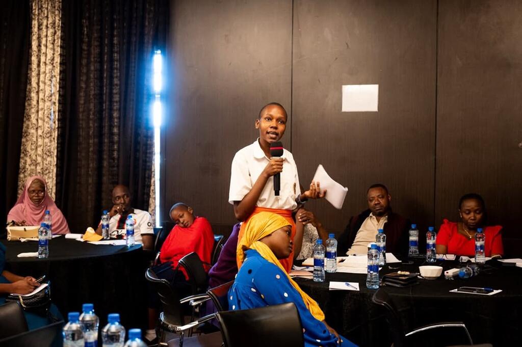 Mwanamke kijana Mwafrika akizungumza kwenye kipaza sauti kwenye meza ya mkutano wakati wa tukio la UNICEF nchini Tanzania.