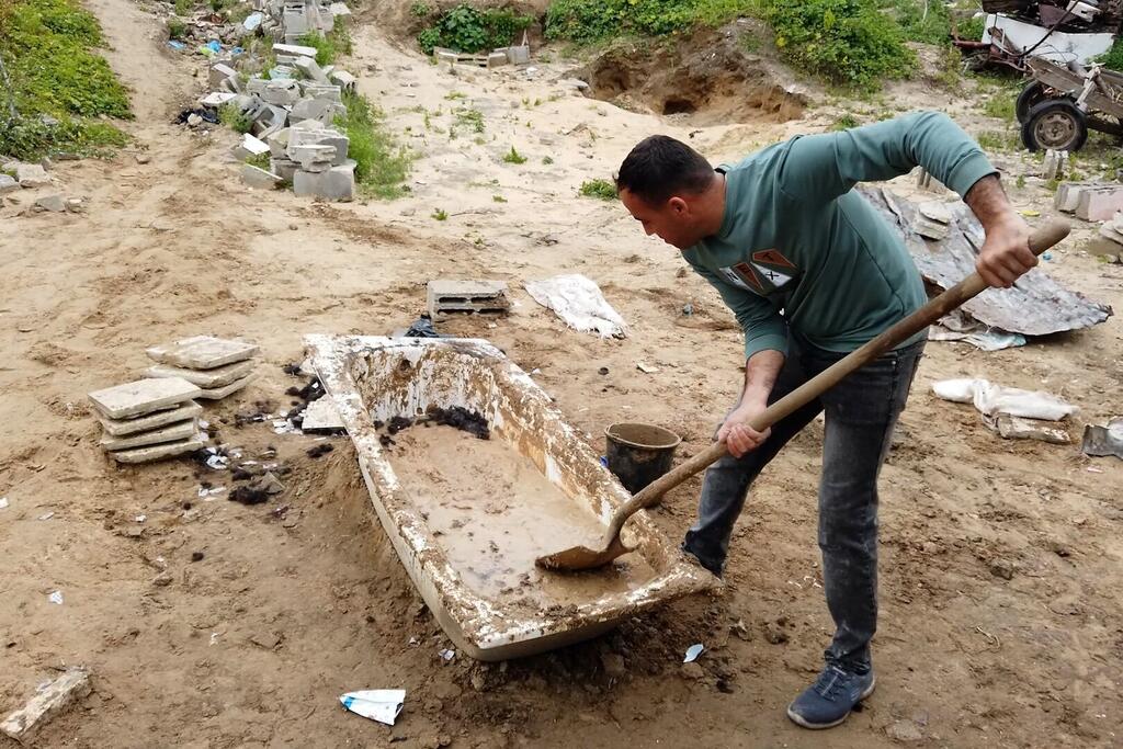رجل فلسطيني يدعى محمد الجثبه يخلط الطين في حوض حمام قديم باستخدام مجرفة في موقع بناء في غزة.