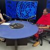 Mwanachama wa UNPFII, Ole Kulet, kutoka Tanzania, anahojiwa na mwanachama wa shirika la Umoja wa Mataifa katika studio yenye nembo za Umoja wa Mataifa nyuma.