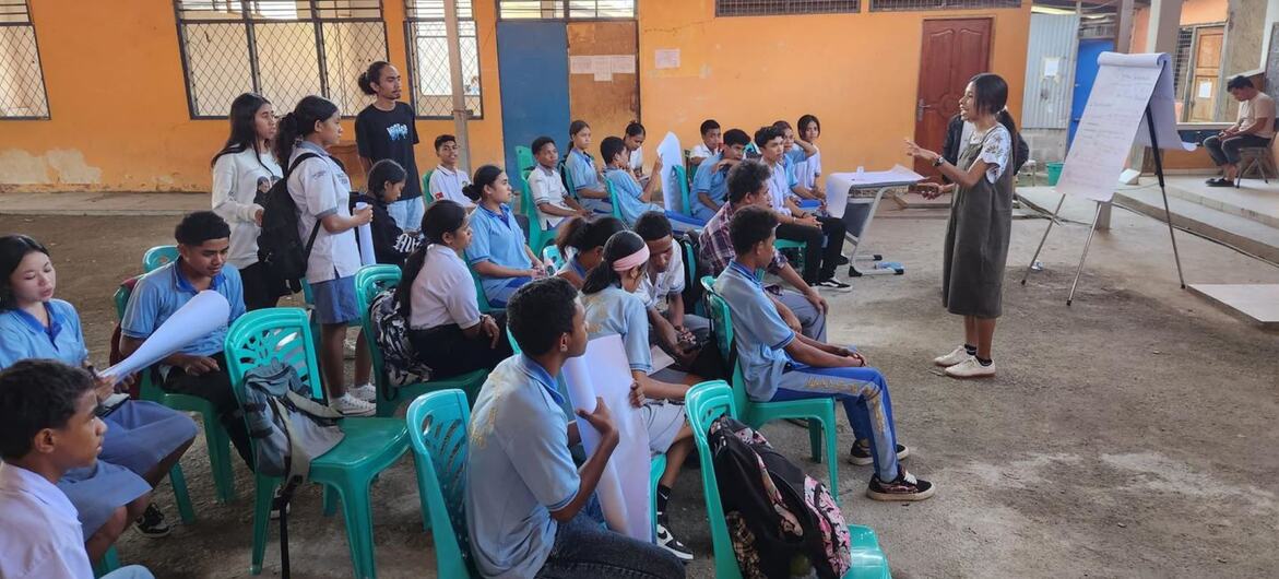Uma mulher, identificada como Joanita Pinto, dirige um workshop ao ar livre para um grupo de jovens como parte do Programa de Integridade da Juventude do PNUD.