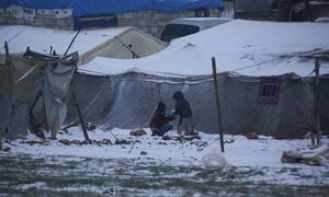 Two children playing in the snow outside a tent in a refugee camp in Syria during winter.