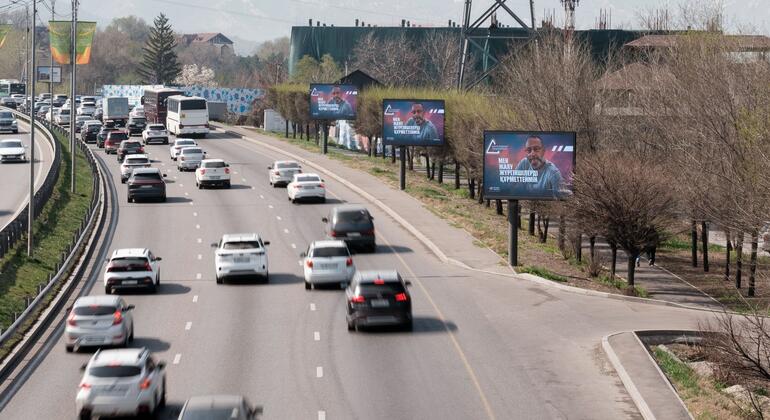 Вид интенсивного движения на многополосной автомагистрали в Казахстане, с несколькими рекламными щитами на обочине дороги.