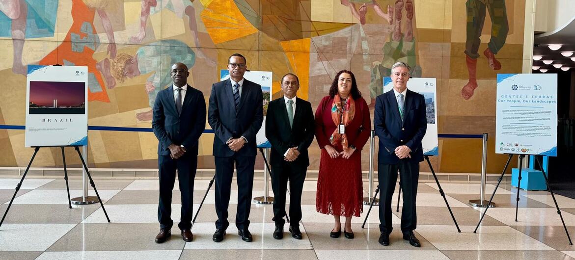 Cinco diplomatas posam para uma foto na exposição da CPLP no saguão da sede da ONU, com painéis visíveis.
