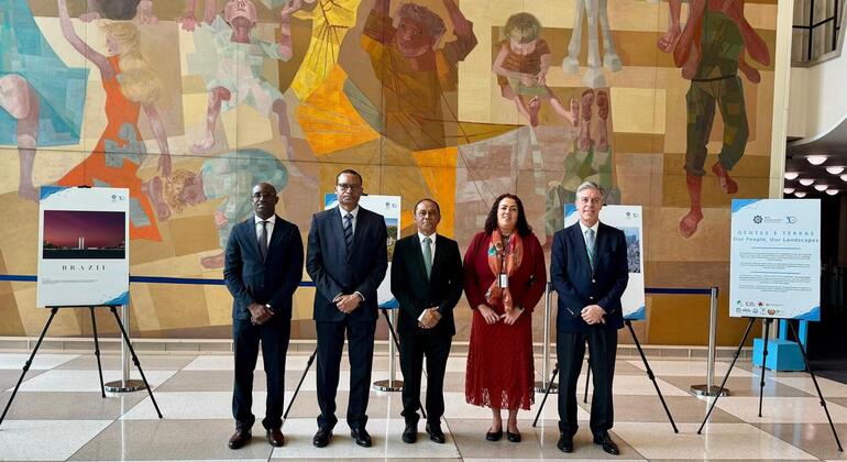Cinco diplomatas posam para uma foto na exposição da CPLP no saguão da sede da ONU, com painéis visíveis.