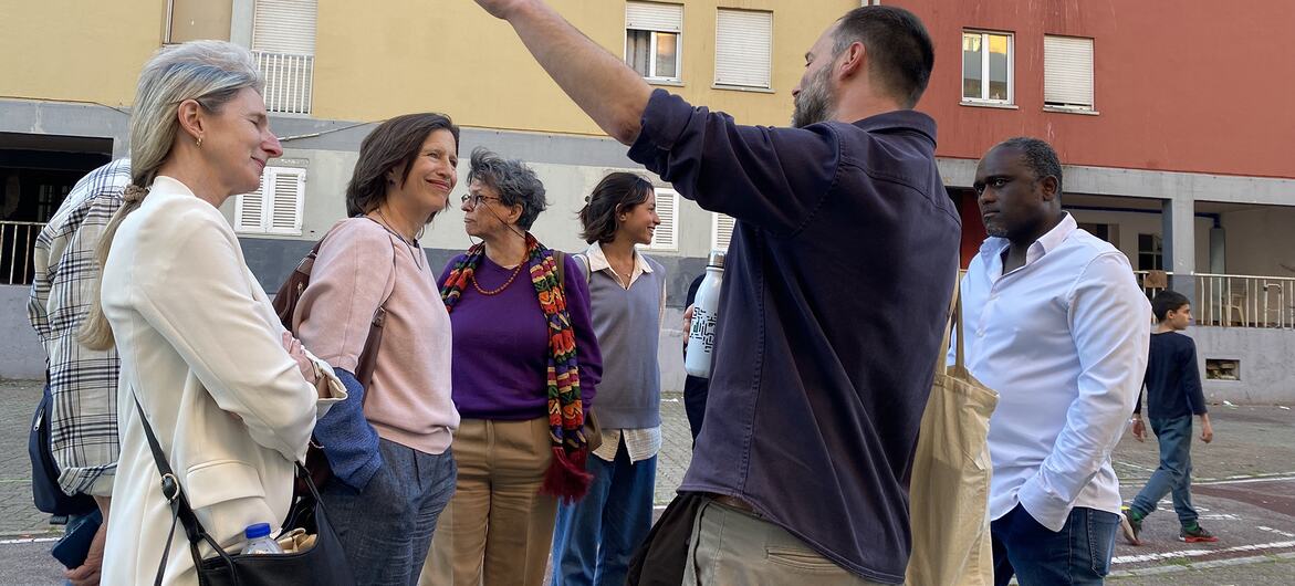 Um grupo de pessoas ouve enquanto um homem faz gestos em direção aos edifícios de Zambujal, Portugal.