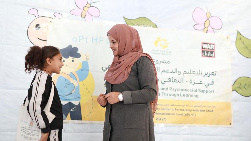Mwalimu mmoja wa Kipalestina aitwaye Salwa akiwa amevaa hijab ya rangi ya waridi anatabasamu huku akishirikiana na msichana mchanga katika nafasi ya kujifunza kwa muda mfupi huko Gaza.