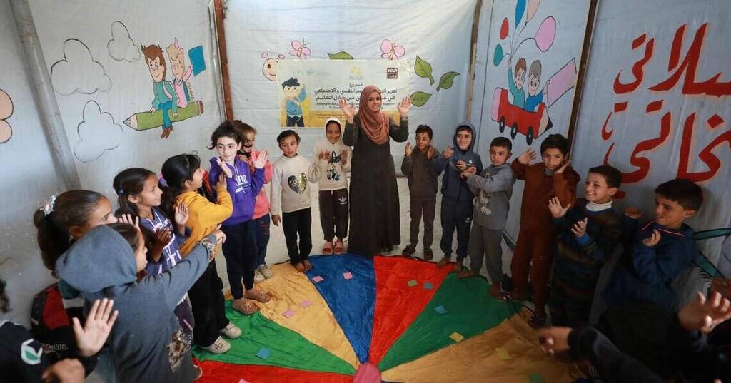 Mwalimu wa kike wa Kipalestina aliyevaa hijab anaongoza kundi la watoto katika shughuli za darasani ndani ya nafasi ya kujifunza kwa muda mfupi huko Gaza.