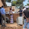 Kikundi cha wanaume na wanawake huko Kigoma, Tanzania, wakichunguza majiko mapya ya chuma katika kijiji cha vijijini.