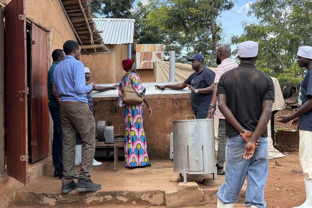 Kikundi cha wanaume na wanawake huko Kigoma, Tanzania, wakichunguza majiko mapya ya chuma katika kijiji cha vijijini.