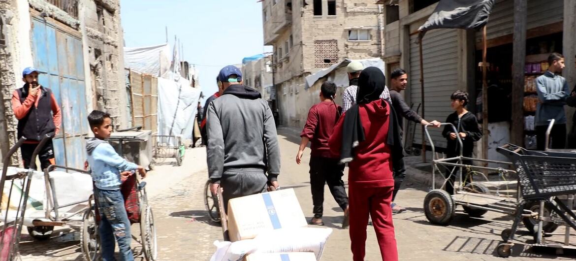 Palestinos carregam caixas de ajuda alimentar em carrinhos e à mão em uma rua de Gaza durante uma distribuição pelo Programa Mundial de Alimentos (PMA).