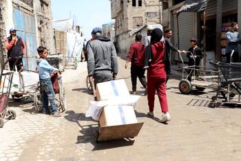 فلسطينيون يحملون صناديق من المساعدات الغذائية على عربات وبيد في شارع في غزة أثناء توزيع من قبل برنامج الأغذية العالمي (WFP).
