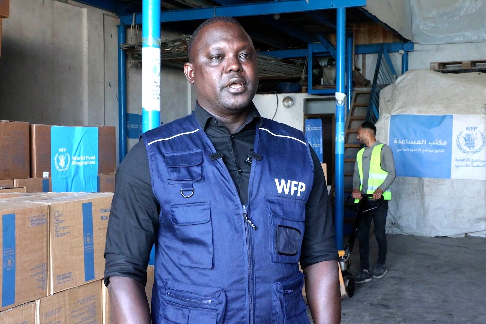 ويلي نييكو ويلي نييكو، منسق الطوارئ ورئيس مكتب برنامج الأغذية العالمي في غزة، يقف في مستودع يحتوي على صناديق مساعدات غذائية مع علامات تجارية من برنامج الأغذية العالمي، يتحدث خلال زيارة لمركز توزيع المساعدات الغذائية.