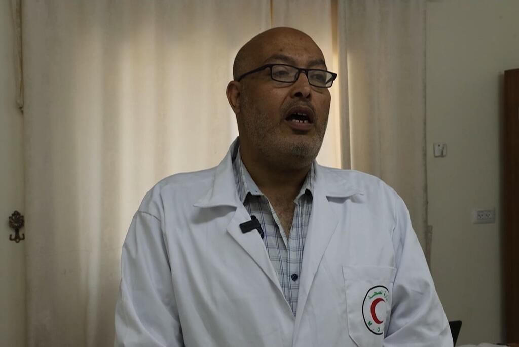 Picha ya karibu ya daktari wa kiume wa Mashariki ya Kati akiwa amevaa miwani na kanzu nyeupe yenye nembo ya Mwezi Mwekundu, akizungumza wakati wa mahojiano.