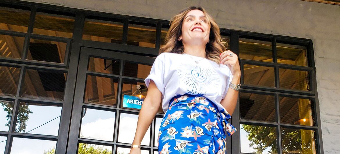 लिना गार्सेस, एक फैशन विशेषज्ञ और शांति समझौते से बची महिला, अन्य महिलाओं के साथ मिलकर बनाई गई इक्सोरा ब्रांड की रंगीन फूलों वाली स्कर्ट को मॉडलिंग करते हुए मुस्कुरा रही हैं।