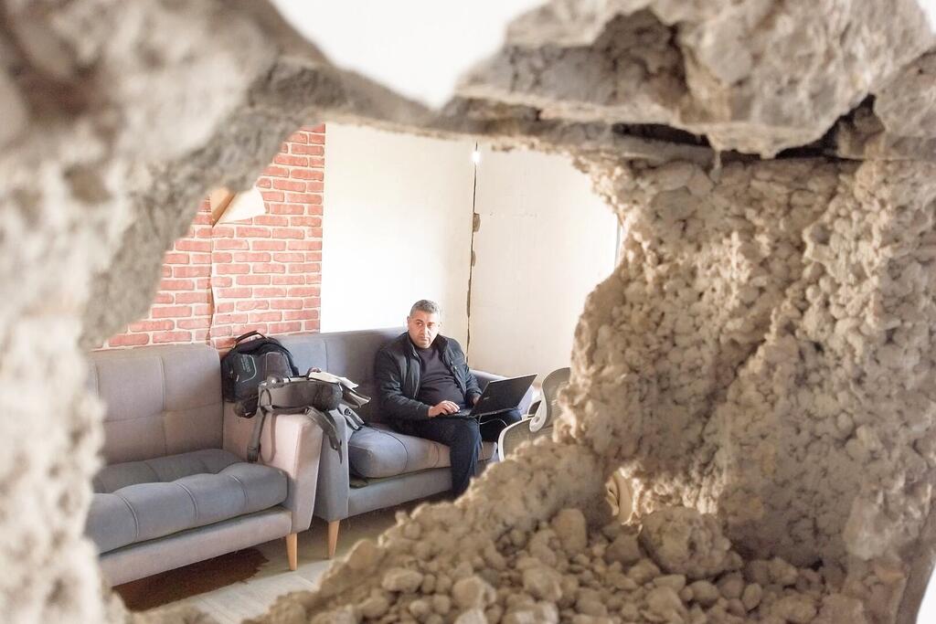 Mwanamume anafanya kazi kwenye kompyuta ndogo ndani ya kituo cha redio kilichoharibiwa huko Gaza, ikionekana kupitia ukuta uliovunjika.