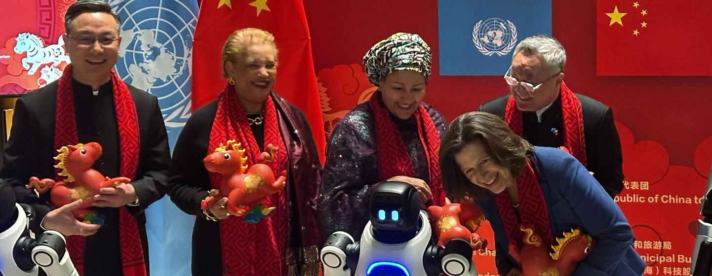 在中国新年庆祝活动中, 一群人和一台机器人, 拿着红色龙雕像, 戴着红色围巾, 背景是中国和联合国的旗.