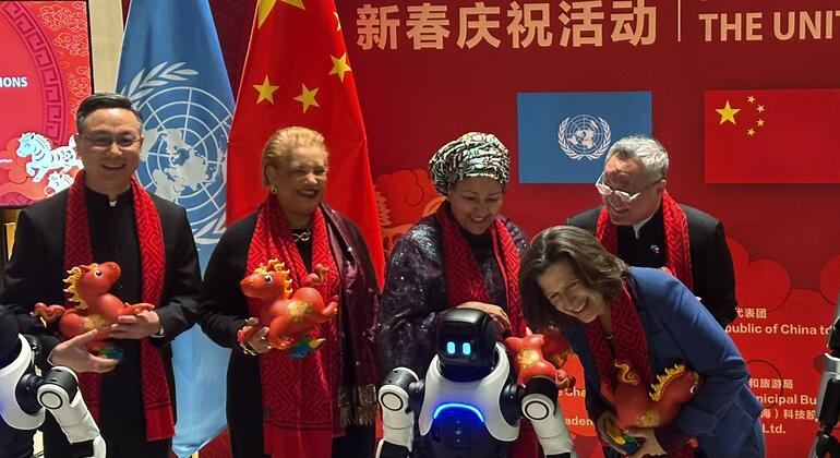 在中国新年庆祝活动中, 一群人和一台机器人, 拿着红色龙雕像, 戴着红色围巾, 背景是中国和联合国的旗.