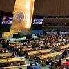 Uma vista panorâmica da sessão setenta da Comissão sobre o Estatuto da Mulher (CSW) na sede das Nações Unidas em Nova York. O grande salão de assembleias está cheio de delegados sentados em mesas curvas voltadas para um pódio central. Dois grandes ecrãs exibem os procedimentos. O emblema da ONU é exibido na parede atrás do pódio.
