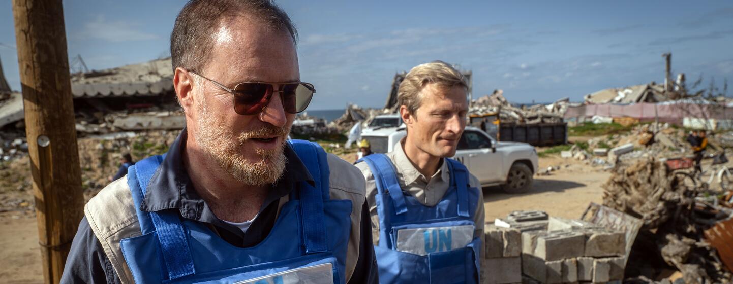 Shaun Hughes, directeur pays du PAM à Gaza, vêtu d'un gilet bleu de l'ONU et de lunettes de soleil, se promène dans un site de destruction et de décombres.