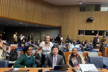 Um grupo de delegados da Namíbia, Mianmar e Moçambique posa para uma foto à mesa de conferências de uma grande sala de reuniões.