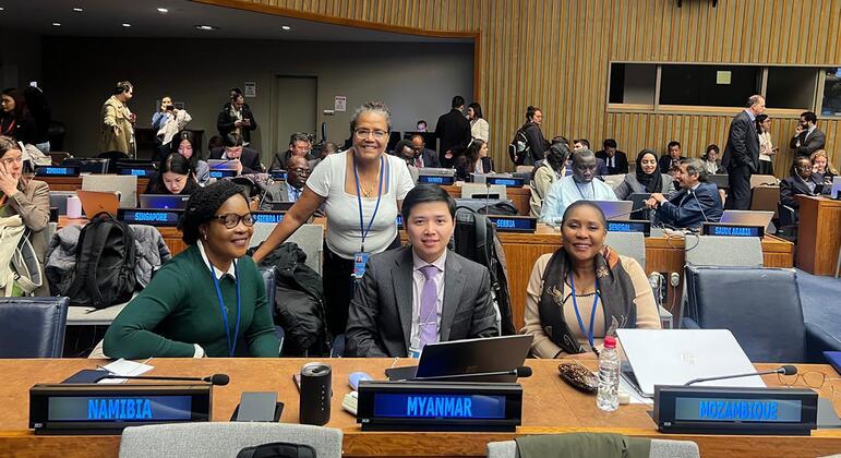 Um grupo de delegados da Namíbia, Mianmar e Moçambique posa para uma foto à mesa de conferências de uma grande sala de reuniões.