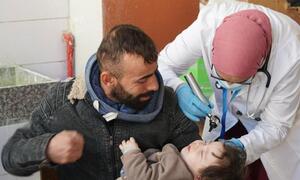 Una doctora con bata blanca y pañuelo rosa examina el oído de un niño dormido con un otoscopio mientras el padre lo sostiene, como parte de una iniciativa de atención médica para personas desplazadas en el Líbano.