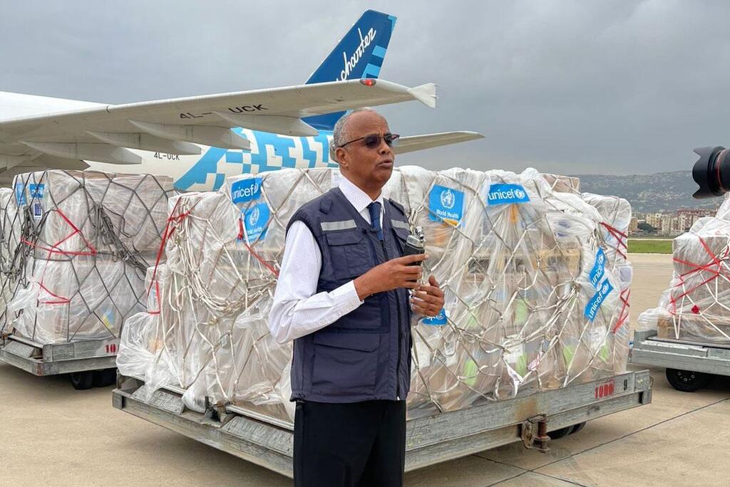 El Dr. Abdinasir Abubakar, Representante de la OMS en el Líbano, se encuentra en la pista de un aeropuerto con carga de suministros de UNICEF y de la OMS detrás de él, frente a un avión fletado.