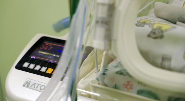 Close-up новорожденного в инкубаторе внутри роддома в Украине, с медицинским оборудованием, показывающим жизненные признаки.