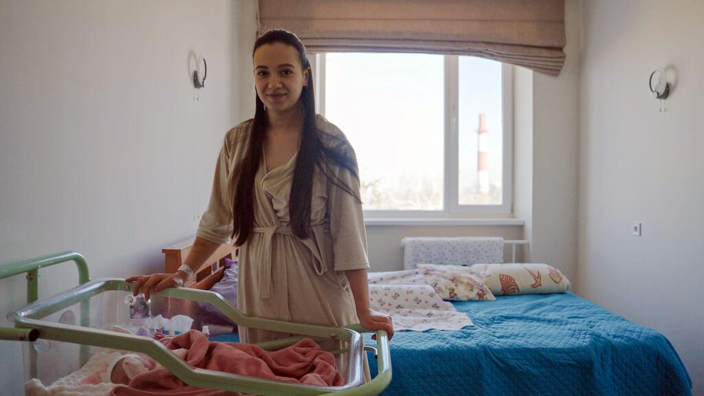 Беременная женщина стоит рядом с новорожденным в инкубаторе внутри роддома в Украине, подчеркивая проблемы, с которыми сталкиваются работники здравоохранения во время продолжающегося конфликта.