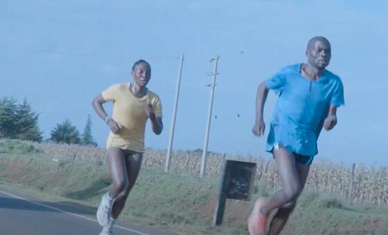 Mwanamume na mwanamke wanakimbia kwenye barabara ya lami kupitia eneo la vijijini nchini Kenya, na mashamba ya mahindi kwenye mandhari ya nyuma.